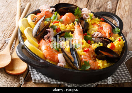 Spanish spicy paella seafood with king prawns, mussels, fish, and baby octopus closeup in a frying pan on wooden background. horizontal Stock Photo