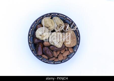 Dried Fruits in an Oriental Bowl. Decorated dish with dried fruit: Figs, dates and natural almonds, Top view, close up, isolated on white background. Stock Photo