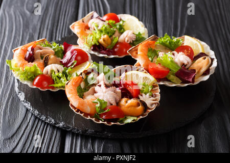 Seafood appetizer salad of shrimp, octopus, mussels, squids and scallops with vegetables and lemon in seashells close-up on a black wooden table. hori Stock Photo