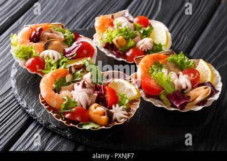 Beautiful seafood cocktail salad of shrimp, baby octopus, mussels, squids and scallops with vegetables in sea shells close-up on a black table. horizo Stock Photo