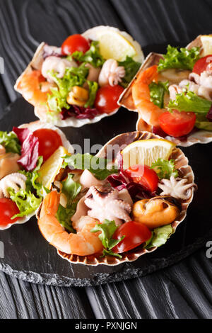 Gourmet seafood salad of shrimp, baby octopus, mussels, squids and scallops in sea shells close-up on the table. vertical Stock Photo