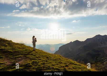 Germany, Bavaria, Oberstdorf, mother and little daughter on a hike in the mountains looking at view at sunset Stock Photo