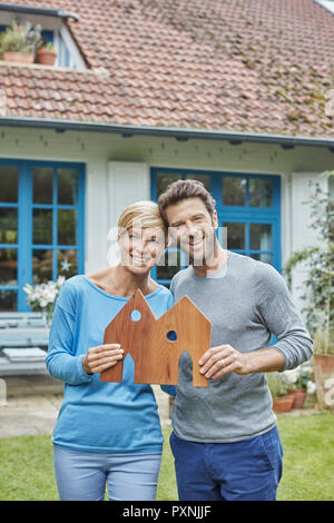 Portrait of smiling couple standing in front of their home holding house model Stock Photo