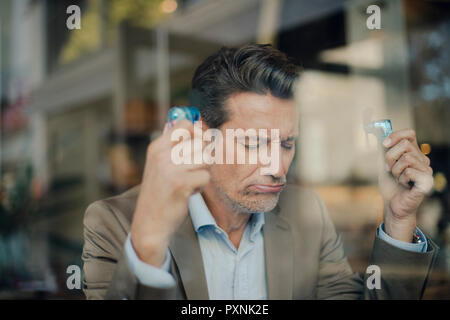 Mature businessman sitting in coffee shop, holding mini fans Stock Photo