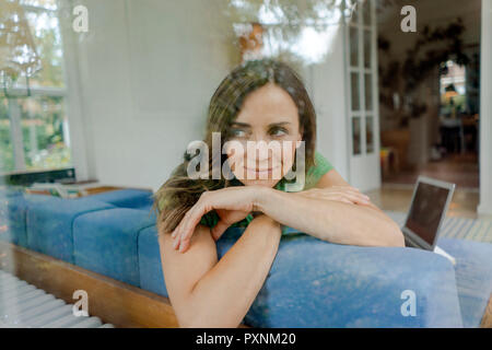 Smiling mature woman on couch at home looking sideways Stock Photo