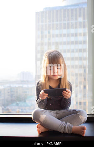 Cute little at home in white room is sitting near window. Stock Photo