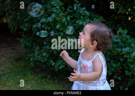 Baby girl watching flying soap bubbles in the garden Stock Photo
