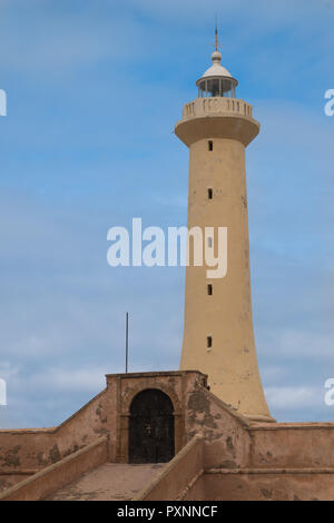 Light color of the tower of lighthouse. Fence with an old gate with an arc. Cloudy sky. Rabat, Morocco. Stock Photo