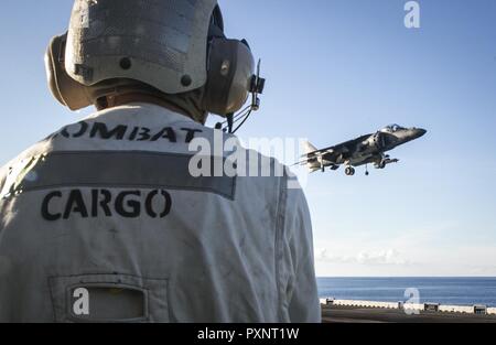 A Marine with combat cargo looks on as an AV-8B Harrier short take off-vertical landing jet prepares to land during deck qualifications aboard the USS Bonhomme Richard (LHD 6) while underway in the Pacific Ocean, June 14, 2017. Marine Attack Squadron 311 and Marine Medium Tiltrotor Squadron 265 (Reinforced) combine to form the Aviation Combat Element of the 31st Marine Expeditionary Unit. The 31st MEU partners with the Navy’s Amphibious Squadron 11 to form the amphibious component of the Bonhomme Richard Expeditionary Strike Group. The 31st MEU and PHIBRON 11 combine to provide a cohesive blue Stock Photo
