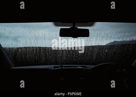 A darkly lit empty car windscreen in the rain - raindrops on windscreen - wet weather car windscreen Stock Photo