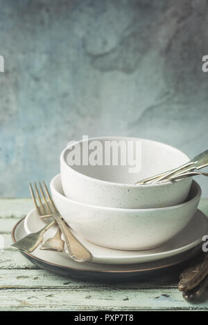 Stack of clean dinner plates with cutlery on top over wooden table. Pastel tones. Stock Photo