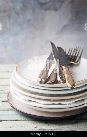 Stack of clean dinner plates with cutlery on top over wooden table. Pastel tones. Stock Photo