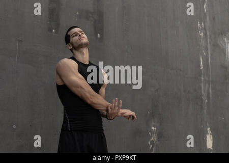 Strong muscular, sporty man warming up, getting ready for training, with a gray urban wall in background. Young sportsman stretching hands and triceps Stock Photo