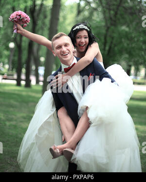 funny groom carries his bride on the back in the Park Stock Photo