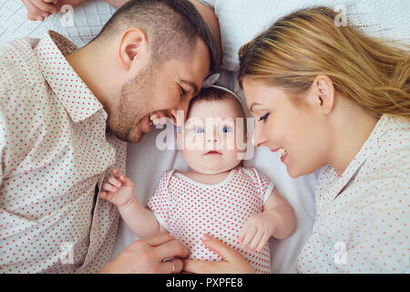 A happy family plays with a toddler on a bed in indoors. Stock Photo