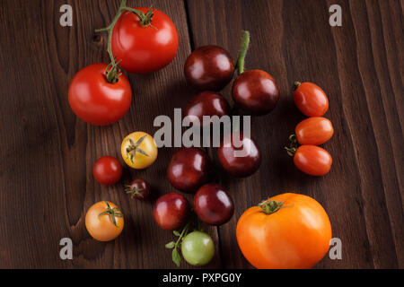 Organic heirloom tomatoes of a variety of sizes and colors, from purple Indigo Rose to red and yellow cherry tomatoes. Artistic still life on dark woo Stock Photo