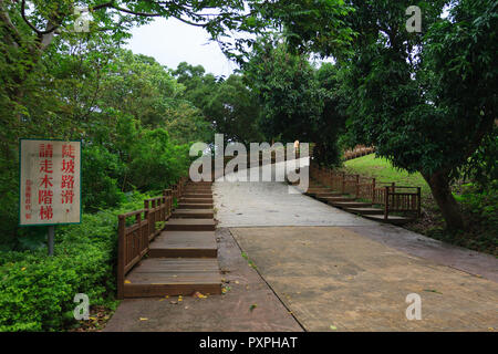 'Slippery steep slope, please walk on wooden stairs' sign. Man walking up wooden footpath surrounded by vegetation, Meilunshan Park, Hualien, Taiwan Stock Photo