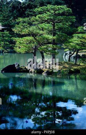 Tranquil scenery of pine trees on an island reflecting in the water of a pond at Rokuon-ji, Kinkaku-ji, Japanese Zen temple garden, Kyoto, Japan. Stock Photo