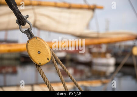 Pulley for sails and ropes made from wood on an old sail boat, with sail and other boats in the harbour, soft and out of focus in the background. Stock Photo