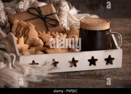 Breakfast tray with a cup of coffee, gingerbread cookies, and hazelnuts candies, a Christmas gift and a woolen scarf, on a rustic wooden table. Stock Photo