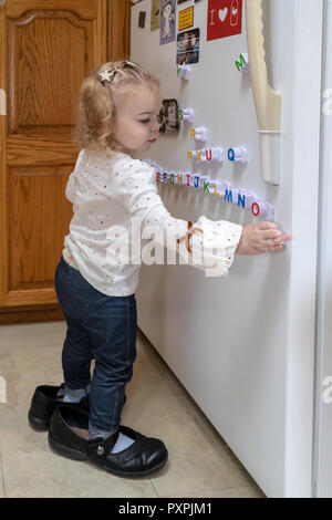 Almost 2 year old girl  wearing Grandma's shoes, at play with magnetic alphabet letters on her refrigerator. Stock Photo