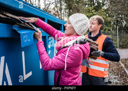 Woman and man putting waste paper in container on recycling center Stock Photo