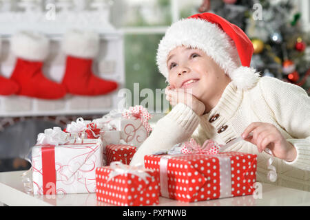 Portrait of cute little boy in Santa hat with gifts for Christmas at home Stock Photo