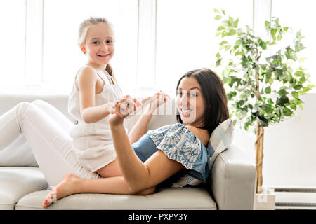Portrait of beautiful mother and her little daughter sitting together on couch Stock Photo