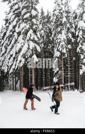 Italy, Modena, Cimone, couple with skiers and snowboard walking in winter forest Stock Photo