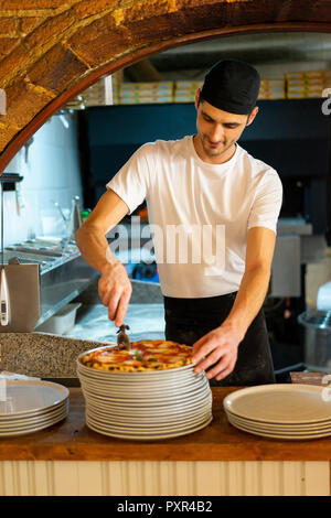 Pizza baker cutting a pizza in kitchen Stock Photo