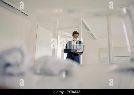Businessman standing in office, using laptop Stock Photo