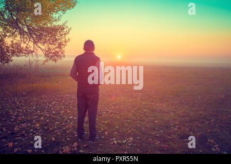 A man stands in the field early in the morning and looks at the sunrise Stock Photo