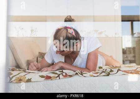 Young woman lying on bed at home writing in diary Stock Photo
