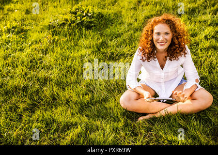 Portrait of happy young woman with tablet relaxing on a meadow Stock Photo