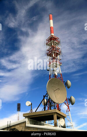 Several kind of communication antennas and a red and white tower against deep mountain blue sky with white clouds Stock Photo