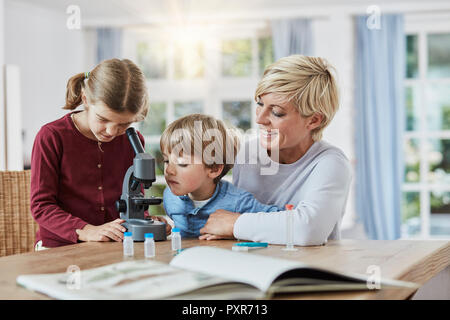 Mother with daughter and son using microscope at home Stock Photo