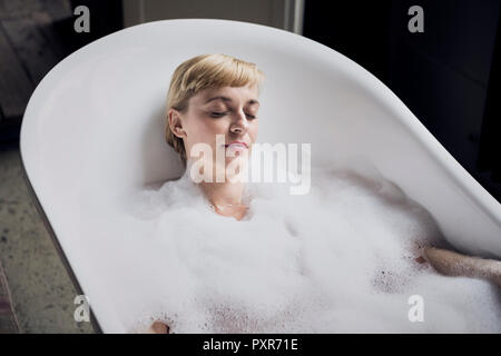 Portrait of woman with eyes closed taking bubble bath in a loft Stock Photo