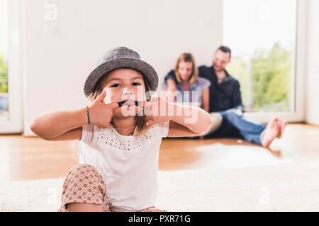 Little girl with hat having fun at home, parents using laptop in background