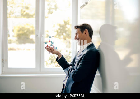 Successful businessman leaning on whiteboard, holding molecule model Stock Photo
