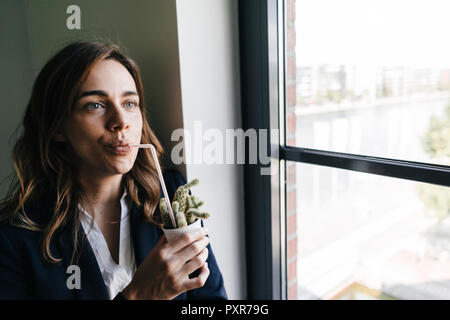 Businesswoman drinking from a straw, sticking in a cactus pot Stock Photo