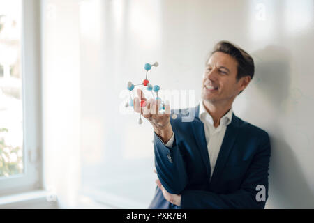 Successful businessman leaning on whiteboard, holding molecule model Stock Photo
