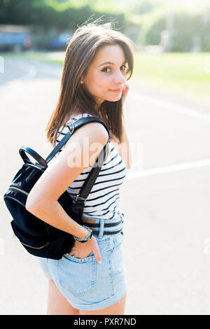 Portrait of smiling young woman with backpack outdoors in summer Stock Photo