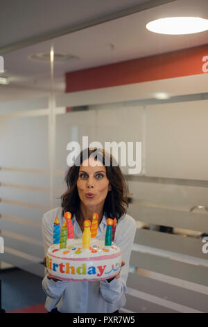 Businesswoman holding birthday cake, blowing out candles Stock Photo