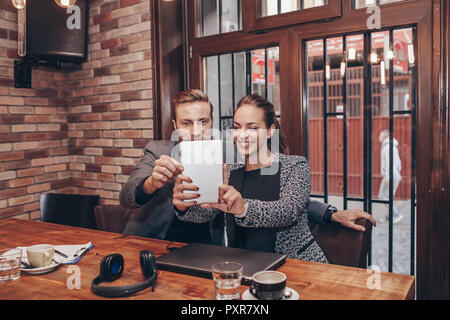 Beautiful young business people are doing selfie using digital tablet and smiling during coffee break Stock Photo