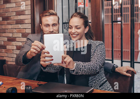 Beautiful young business people are doing selfie using digital tablet and smiling during coffee break Stock Photo