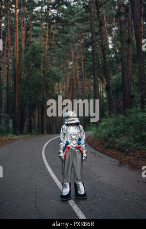 Spaceman exploring nature, standing on road in foreat Stock Photo