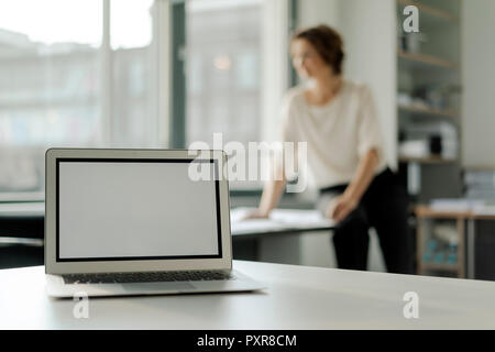 Laptop on shelf, businesswoman working in background Stock Photo