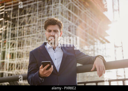 Businessman standing on bridge in front of construction site using cell phone Stock Photo