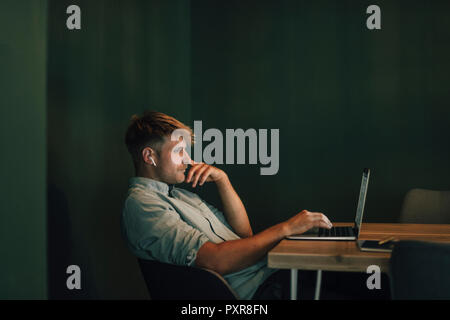 Man sitting in office, working late in his start-up company, listening music Stock Photo