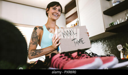 Smiling young woman looking at camera with fan mail box in hand. Female vlogger making mail time video at home Stock Photo
